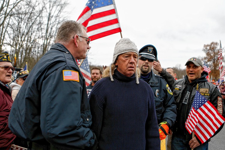 Campus police escort a man away from a Nov. 27, 2016 protest at Hampshire College in reaction to the school's decision to hold off on hoisting the flag in the center of the Amherst campus. The school removed the U.S. flag indefinitely after, since Election Day, it has been set ablaze, replaced, and lowered to half-staff. The man was interrupting speeches and hoisting a sign with offensive language. —GAZETTE STAFF/SARAH CROSBY